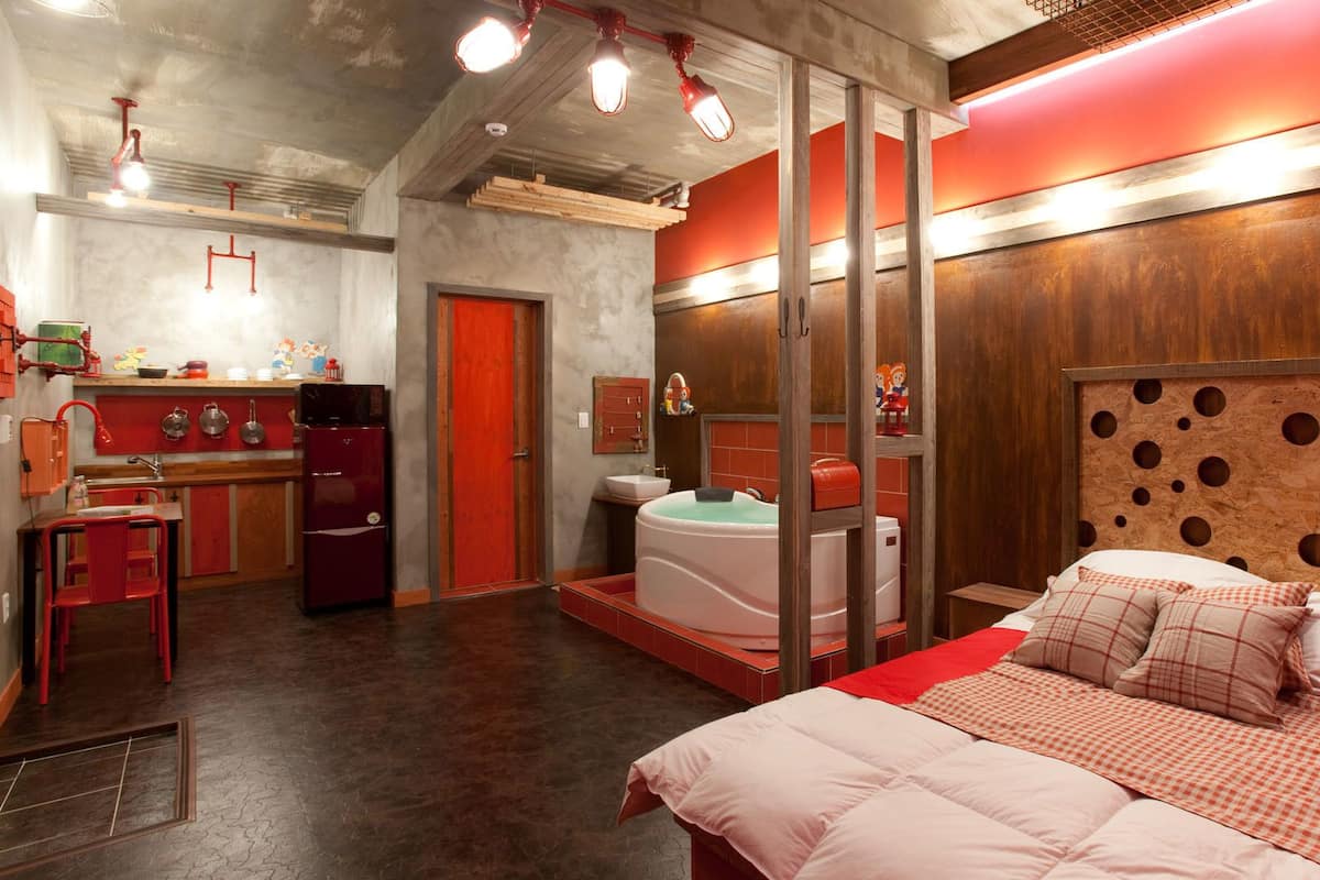 A modern hotel room with a large bed, a separate bathroom, and a kitchenette.