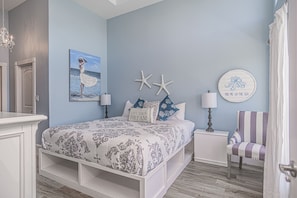 Een slaapkamer met een bed, nachtkastjes, een stoel en decoraties aan de muur, waaronder zeesterren en een schilderij.