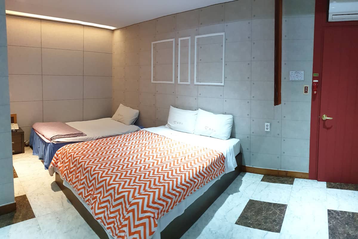 A hotel room with a bed, a nightstand, a red door, and a wall-mounted air conditioner.