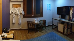 Camera d'albergo con pavimento in legno, una scrivania con computer, televisore, finestra vista e condizionatore d'aria a parete.
