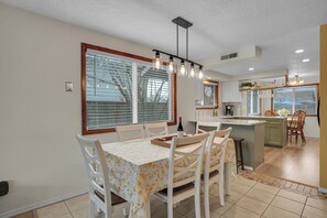 Una cocina moderna con una isla central, armarios blancos y un comedor con mantel floral.