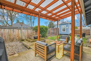 Un patio techado con mobiliario de madera, una mesita y un cobertizo azul al fondo.