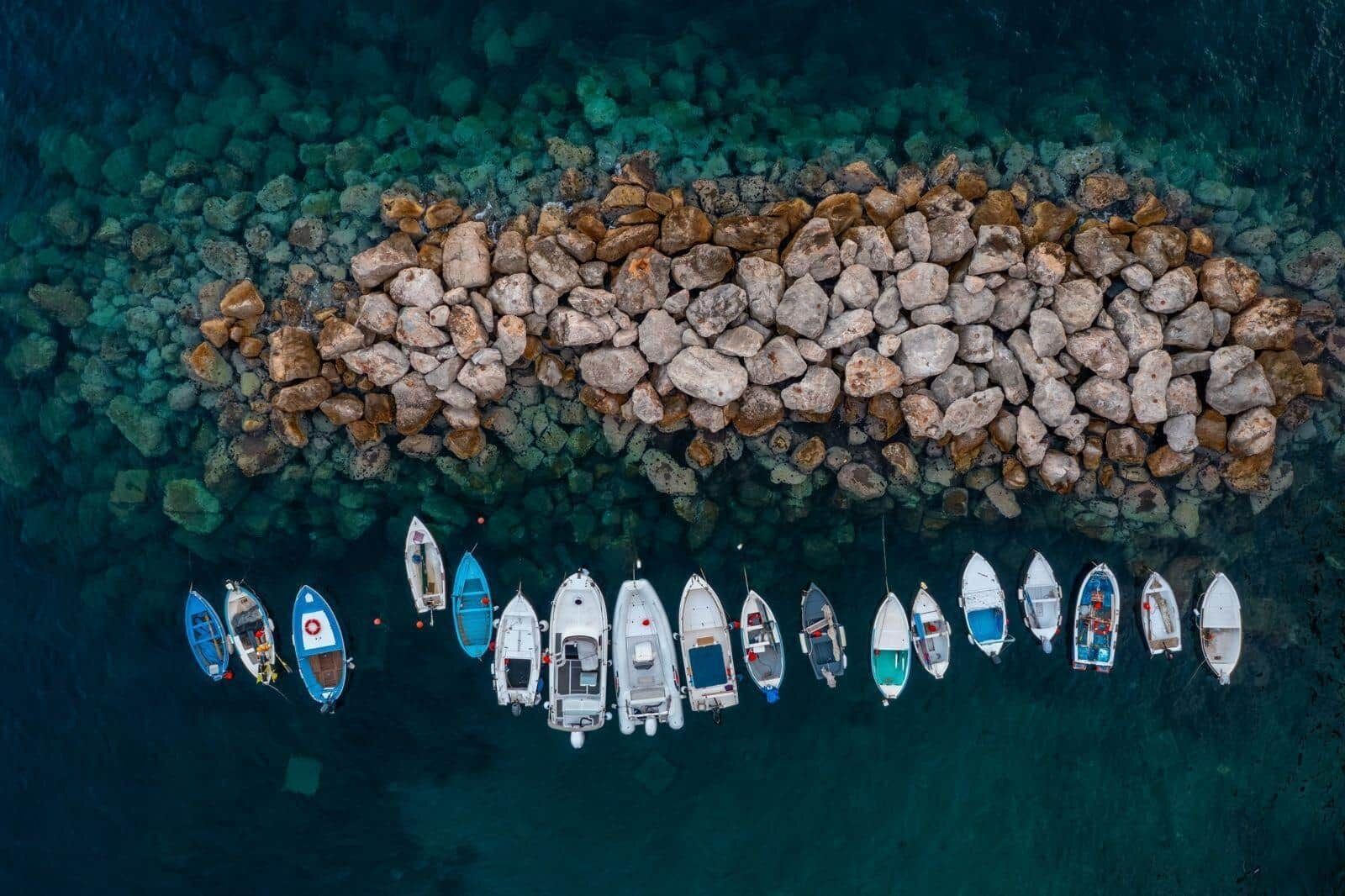 An aerial view of a rocky shoreline with several small boats docked in a row.