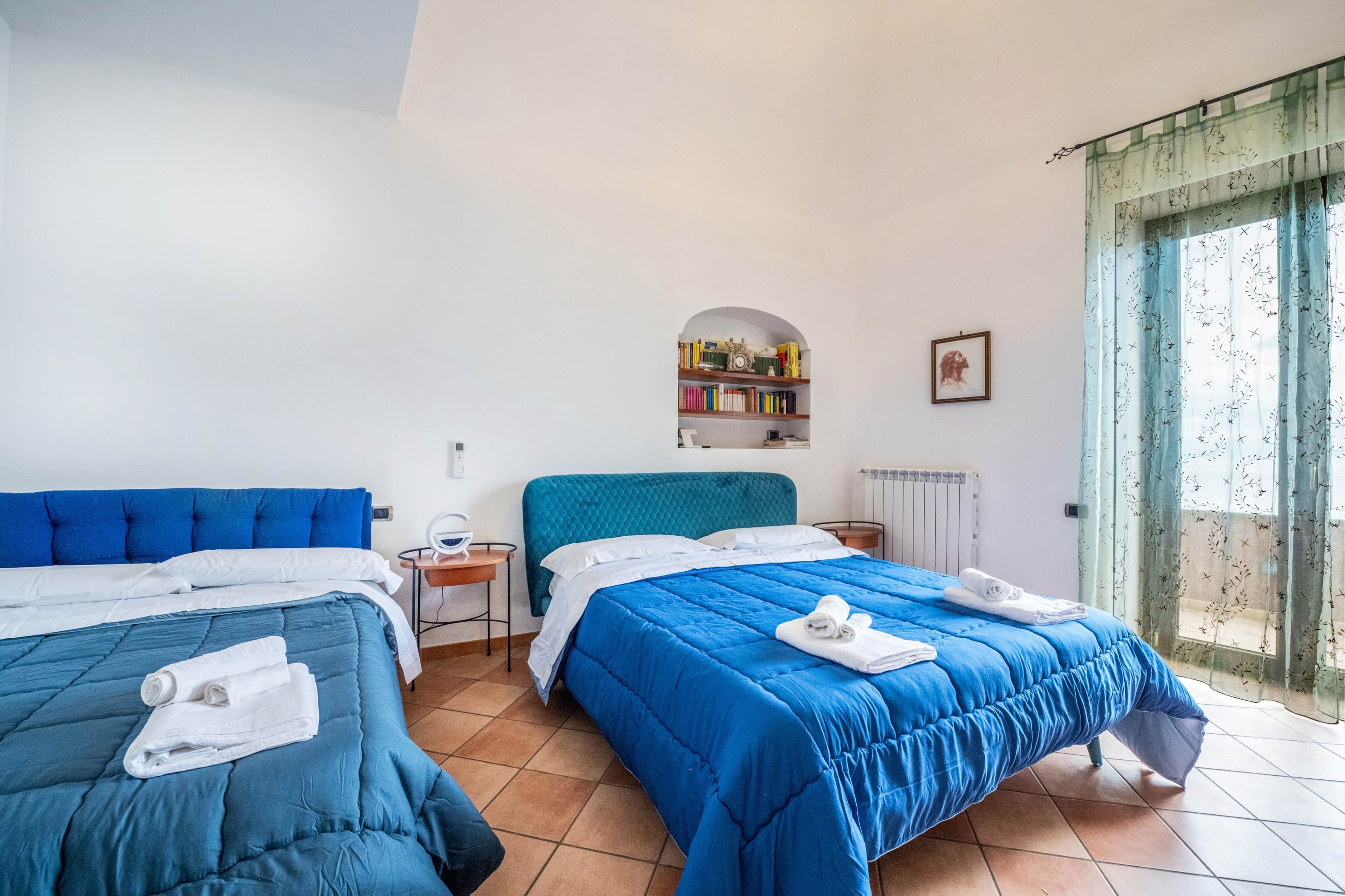 Une chambre d’hôtel avec deux lits, une petite table de chevet, une bibliothèque et une fenêtre avec des rideaux.