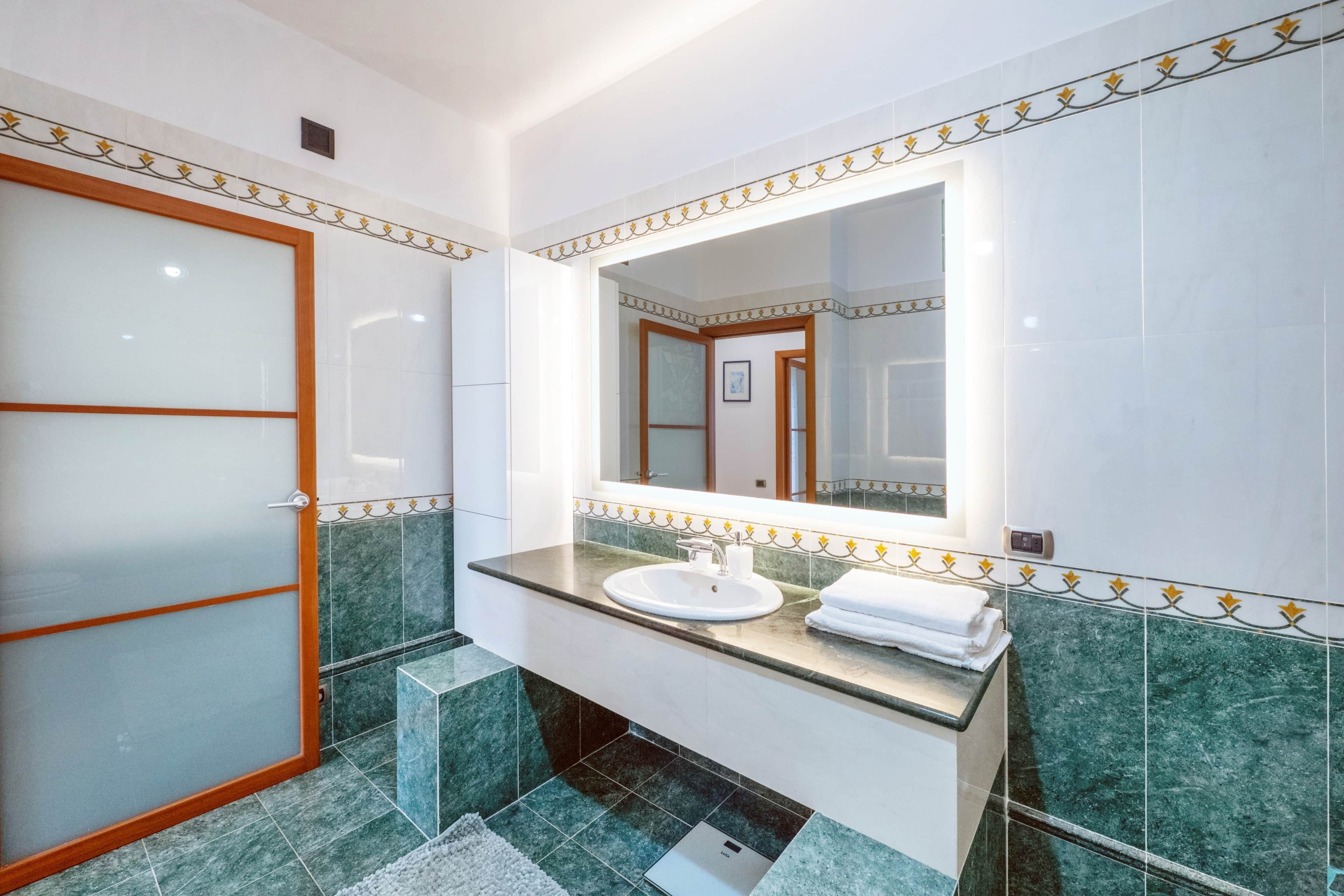 A modern bathroom with a glass door shower, a sink with a mirror, and a tiled floor.