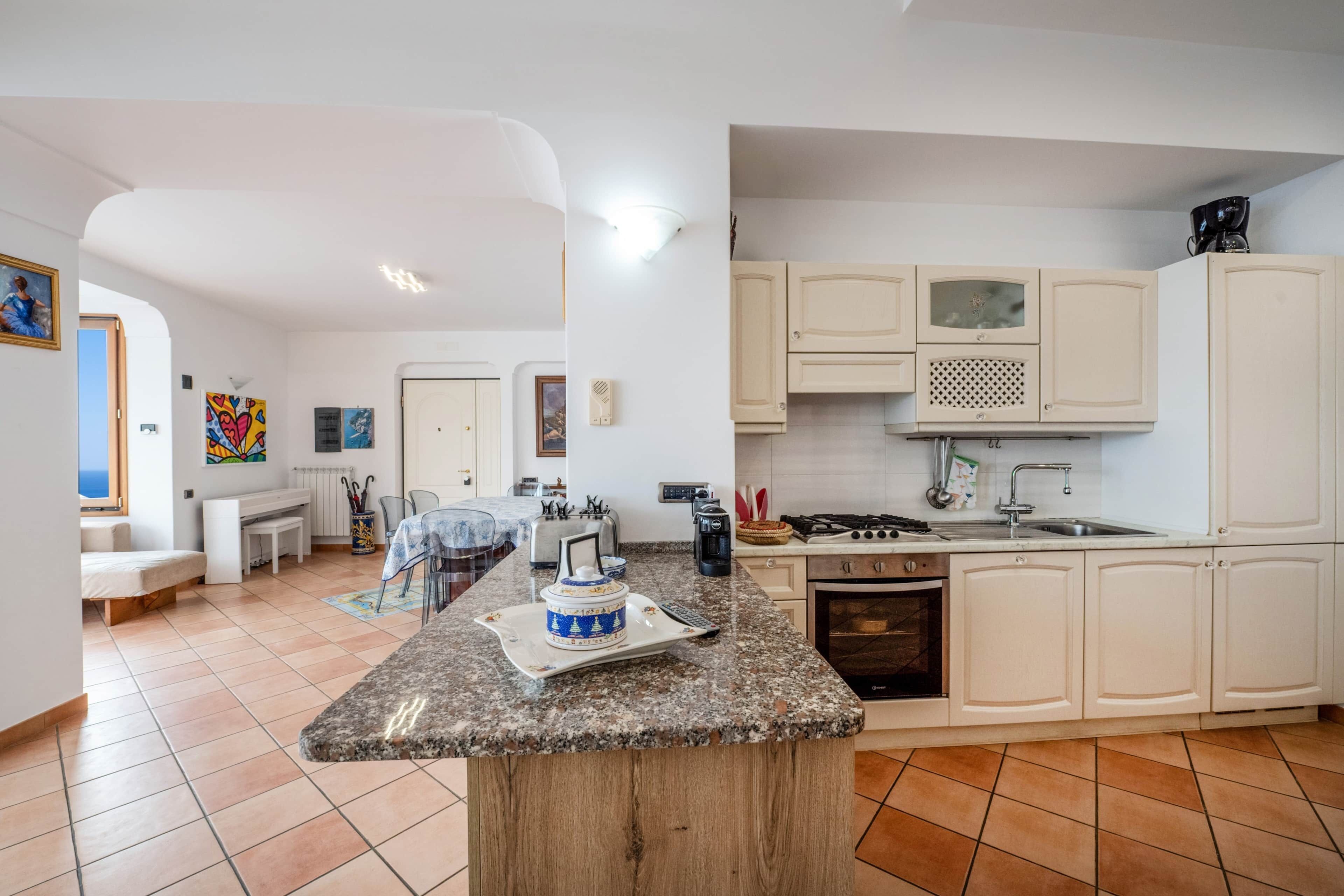 Une cuisine moderne dotée d’un plan de travail en granit, de meubles blancs, d’une cuisinière et d’un coin repas avec une table et des chaises.