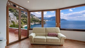 A room with a large sliding glass door leading to a balcony with a view of a coastal landscape. - Il Sogno Costa d’Amalfi - Sea View Apartment (Conca dei Marini)
