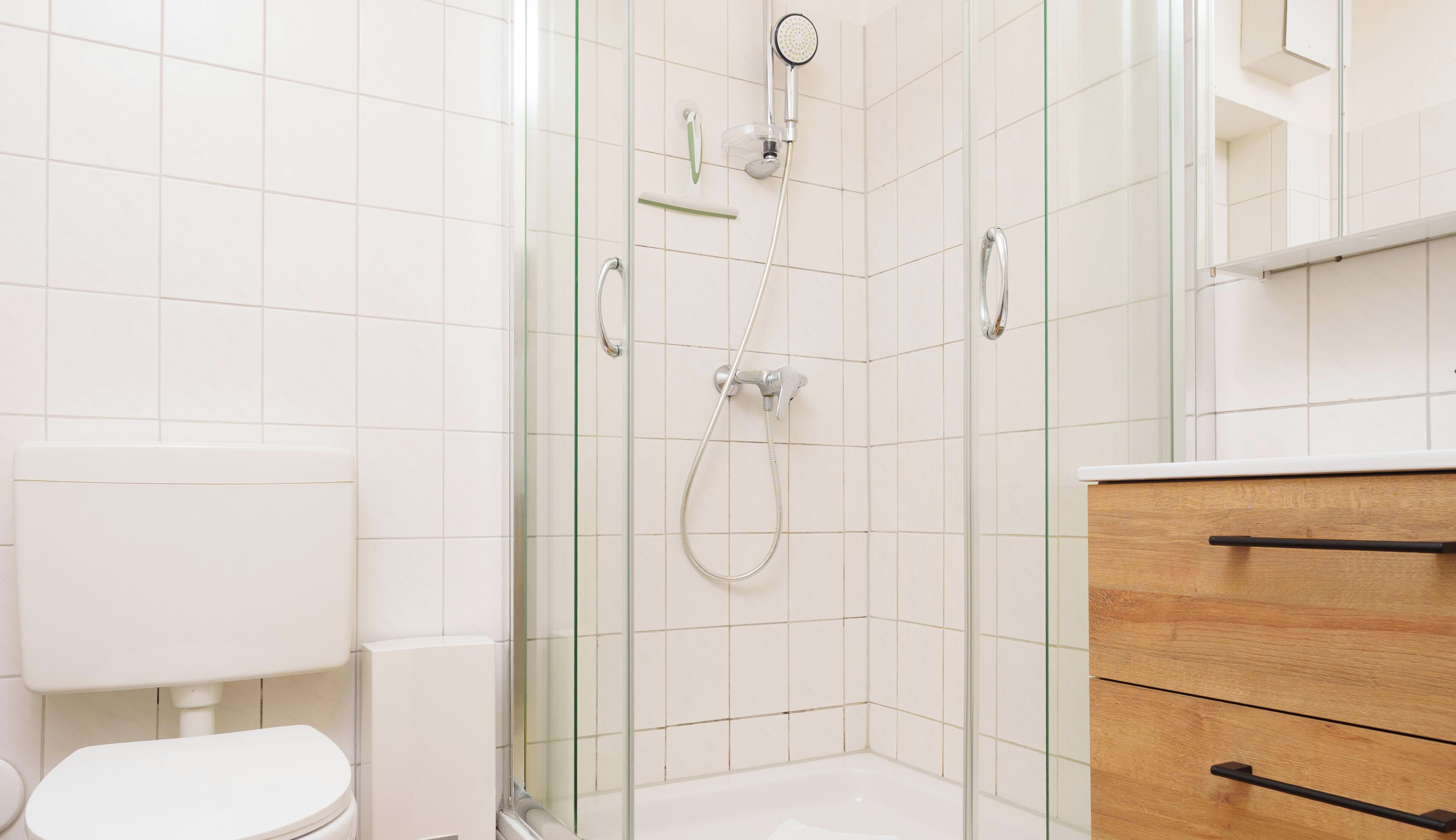 Ein Badezimmer mit einer Duschkabine aus Glas, einer Toilette und Holzschränken.