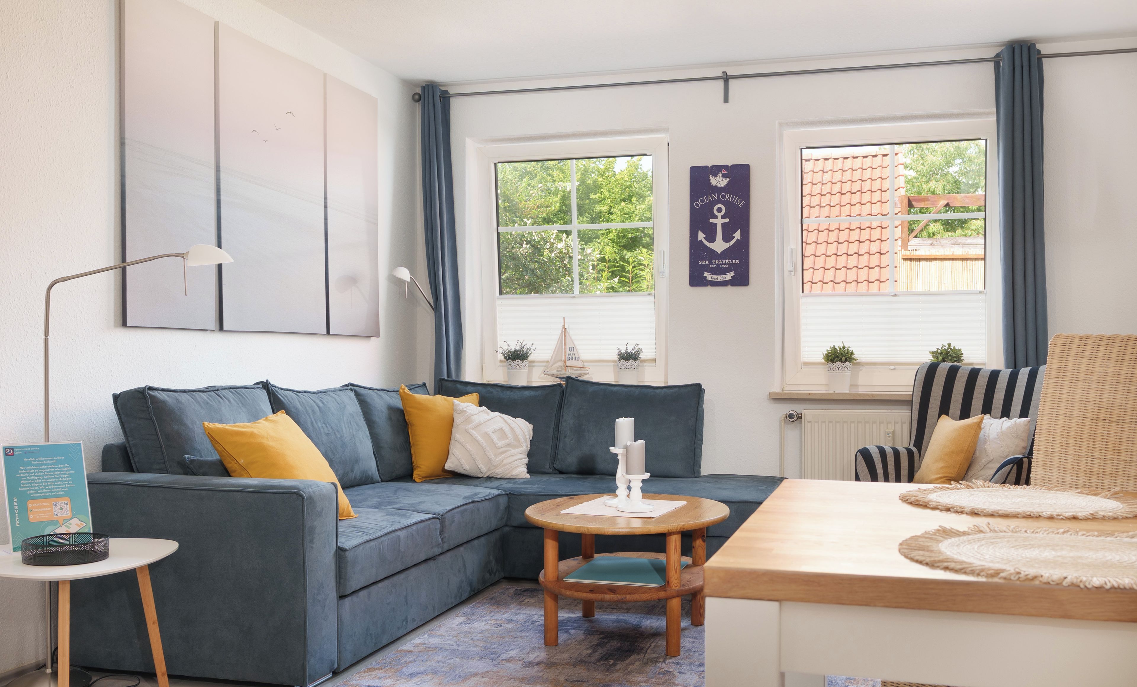 Ein modernes Wohnzimmer mit einem grauen Sofa, einem runden Holztisch und Blick ins Freie durch große Fenster.