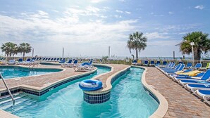 A pool area with multiple swimming pools, lounge chairs, and palm trees. - Bay Watch Resort 419 - Beautiful North Myrtle Beach Oceanfront 1 Bedroom 1 Bath (North Myrtle Beach)