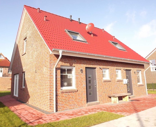 A single-story brick building with a red tiled roof, two skylights, and a small front porch with a bench. - Vacation cottage Nixe, Germany (Wittmund)