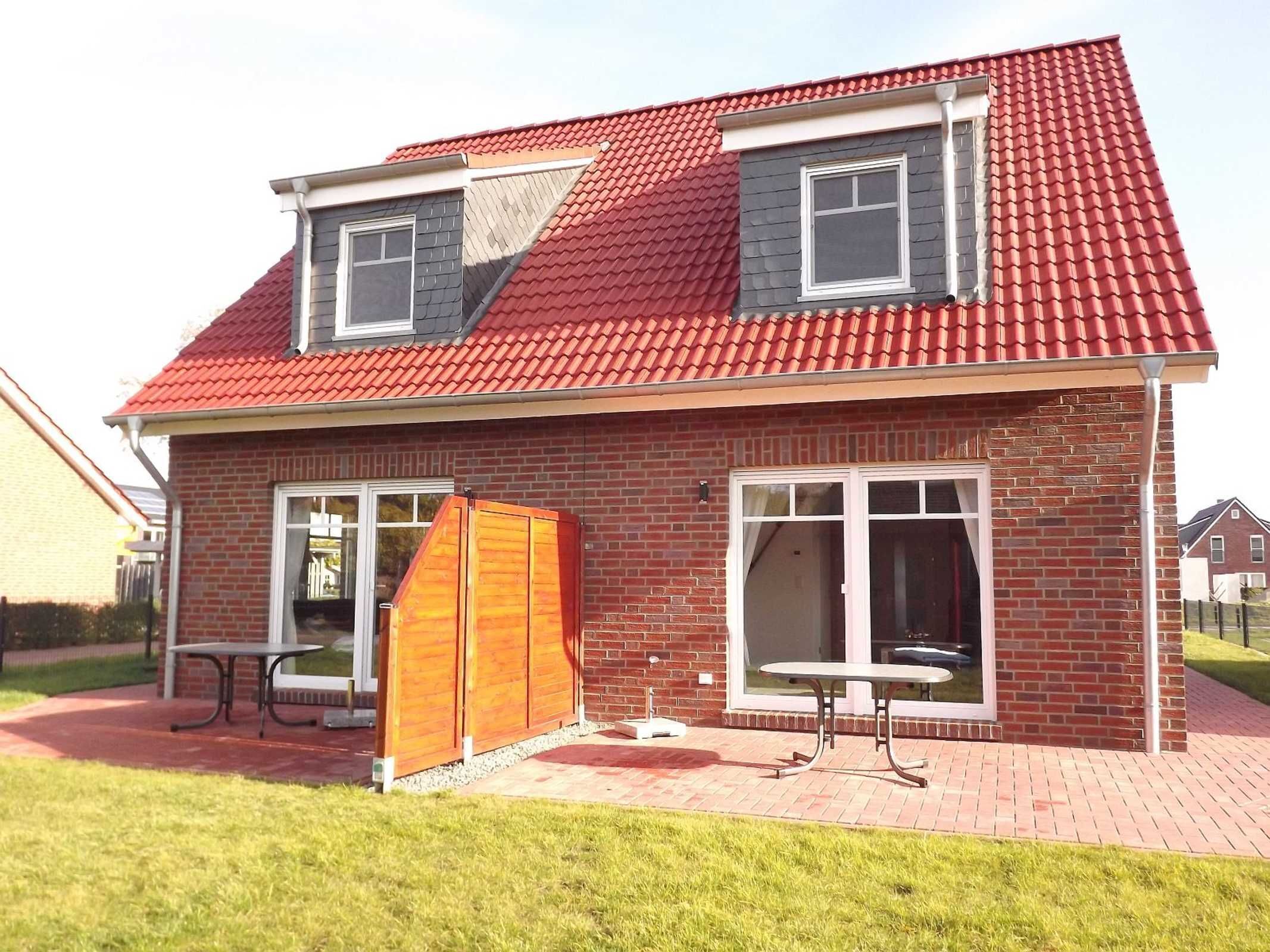 A two-story house with a red-tiled roof, brick exterior, and a small patio area with a table and chairs.