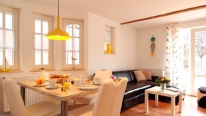 A bright, well-lit room with a dining table set for breakfast, a black leather sofa, and a small white table. - Shell Whg. dolphin, Germany (Ostseebad Boltenhagen)