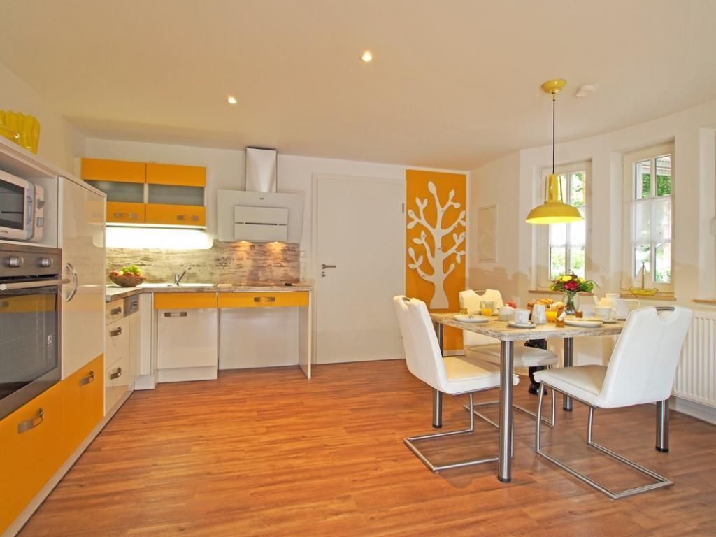 A modern kitchen with yellow and white cabinets, a dining area with white chairs, and a large window with a view of greenery.