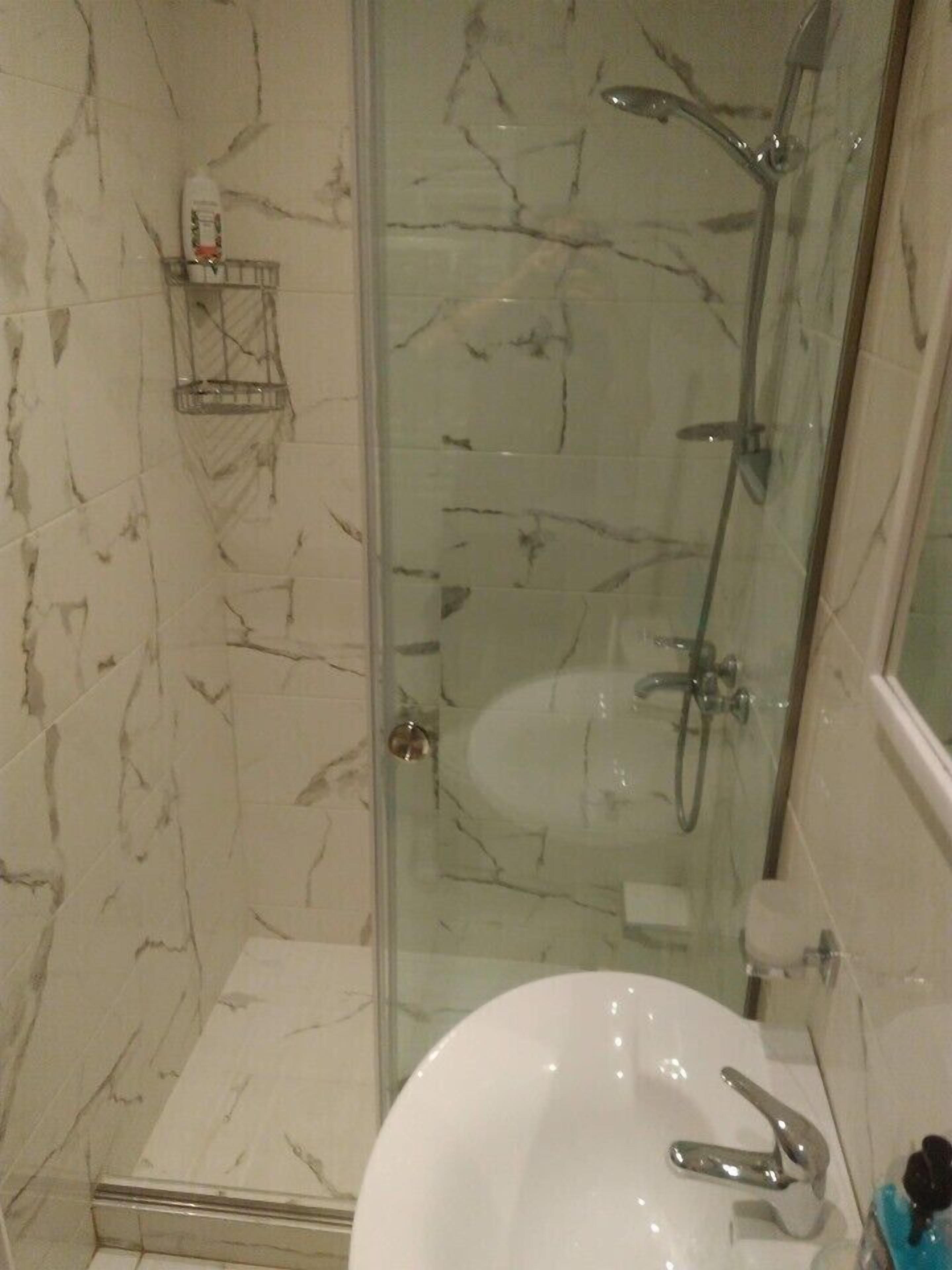 A bathroom with a glass-enclosed shower, a white sink, and a marble-tiled wall.