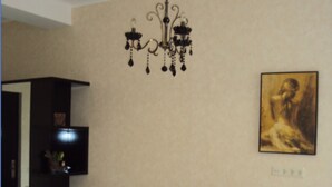 A living room with a brown sofa, two yellow cushions, a black entertainment unit, and a chandelier. - Apartments in front of the Park (Tbilisi)