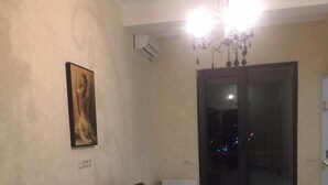 A living room with a brown sofa, a chandelier, and a painting on the wall. - Apartments in front of the Park (Tbilisi)