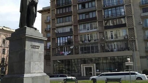 Eine Statue vor einem mehrstöckigen Gebäude mit Balkonen und großen Fenstern.