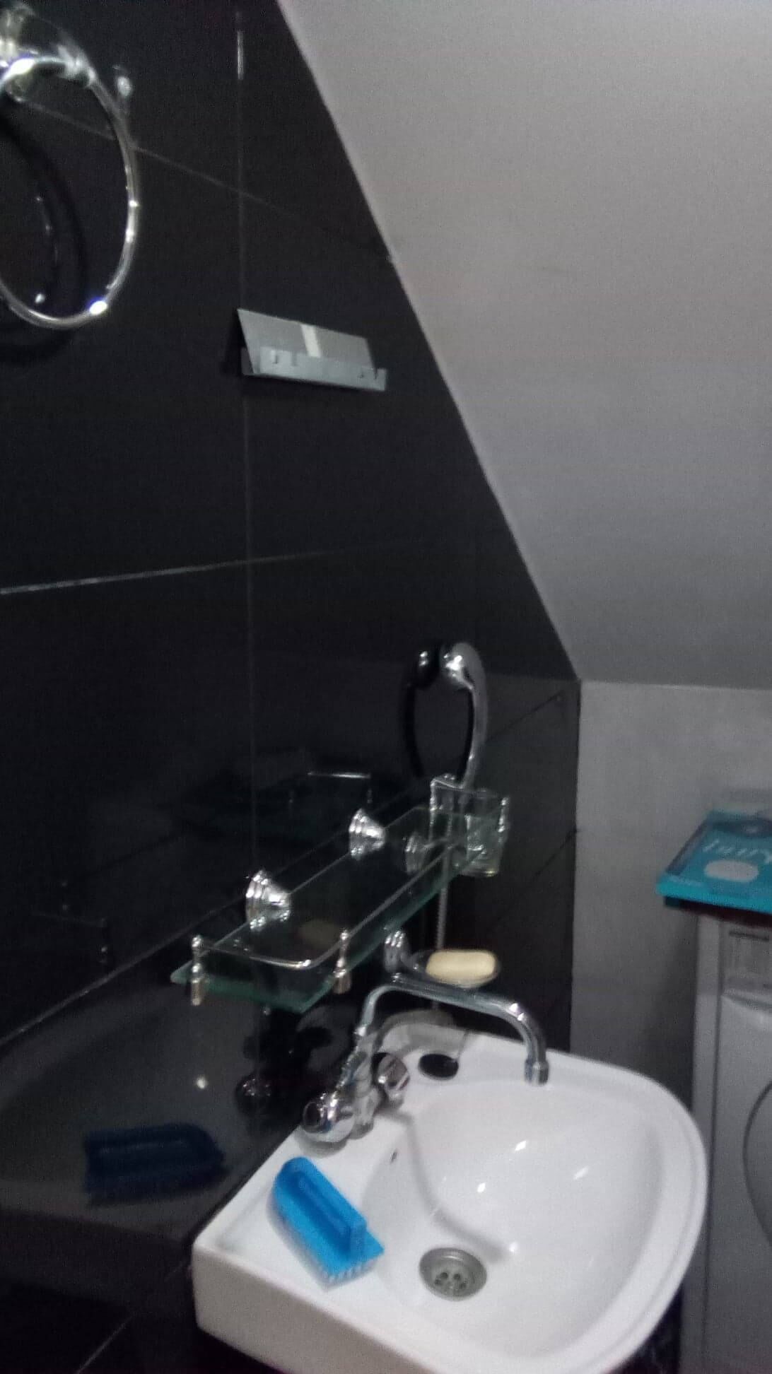 Ein Badezimmer mit einem weißen Waschbecken, einer Glas-Seifenschale, einem blauen Schwamm und einem chromfarbenen Wasserhahn.