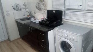 Pieni, käytännöllinen keittiö, jossa on pesuallas, liesi ja pyykinpesukone.