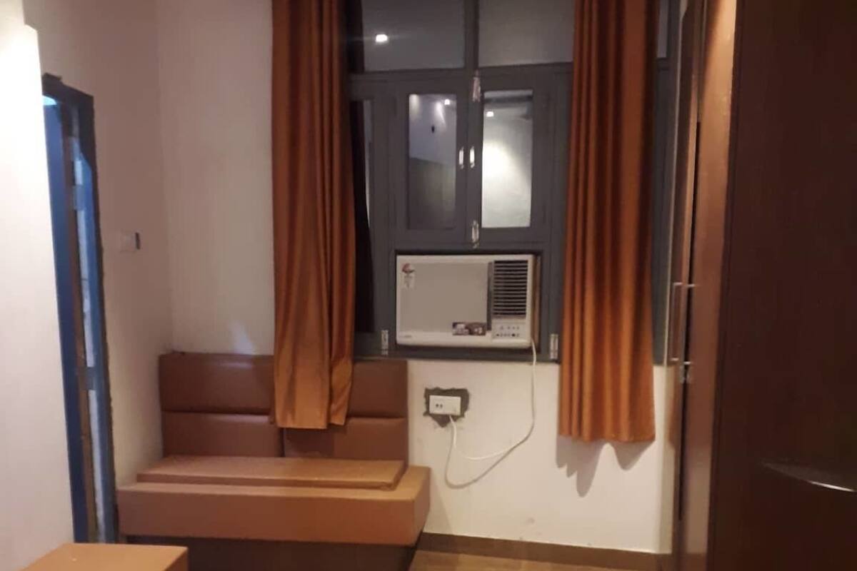A compact room with a bed, a small table, a built-in bench, and a window with curtains.