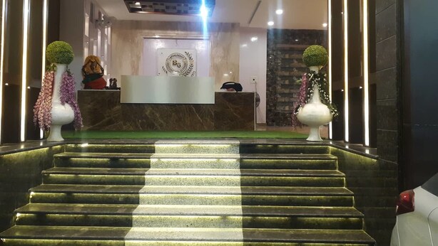 A hotel lobby with a marble reception desk, a staircase leading to the upper floor, and decorative vases with greenery. - Banaras Hotel LLP (Kanpur)