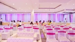 A banquet hall with rows of white chairs and tables, pink sashes, and a ceiling with recessed lighting. - Banaras Hotel LLP (Kanpur)
