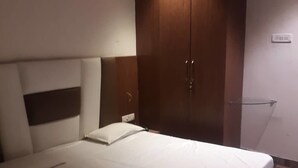 A bedroom with a large bed, wooden wardrobe, and a nightstand. - Banaras Hotel LLP (Kanpur)
