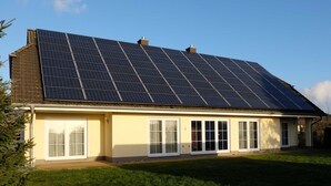 A house with a large solar panel array on the roof and a front porch with white-framed windows.