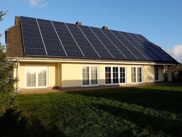 A house with a large solar panel array on the roof and a front porch with white-framed windows.