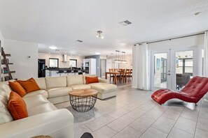 A modern living room with a sofa, a red chair, and a dining area with chairs and a table.