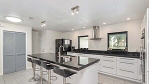 A modern kitchen with a central island, bar stools, stainless steel appliances, and a window providing a view. - Vacation Home With A Stunning View - 870 3 Bedroom Home by RedAwning (Inverness)