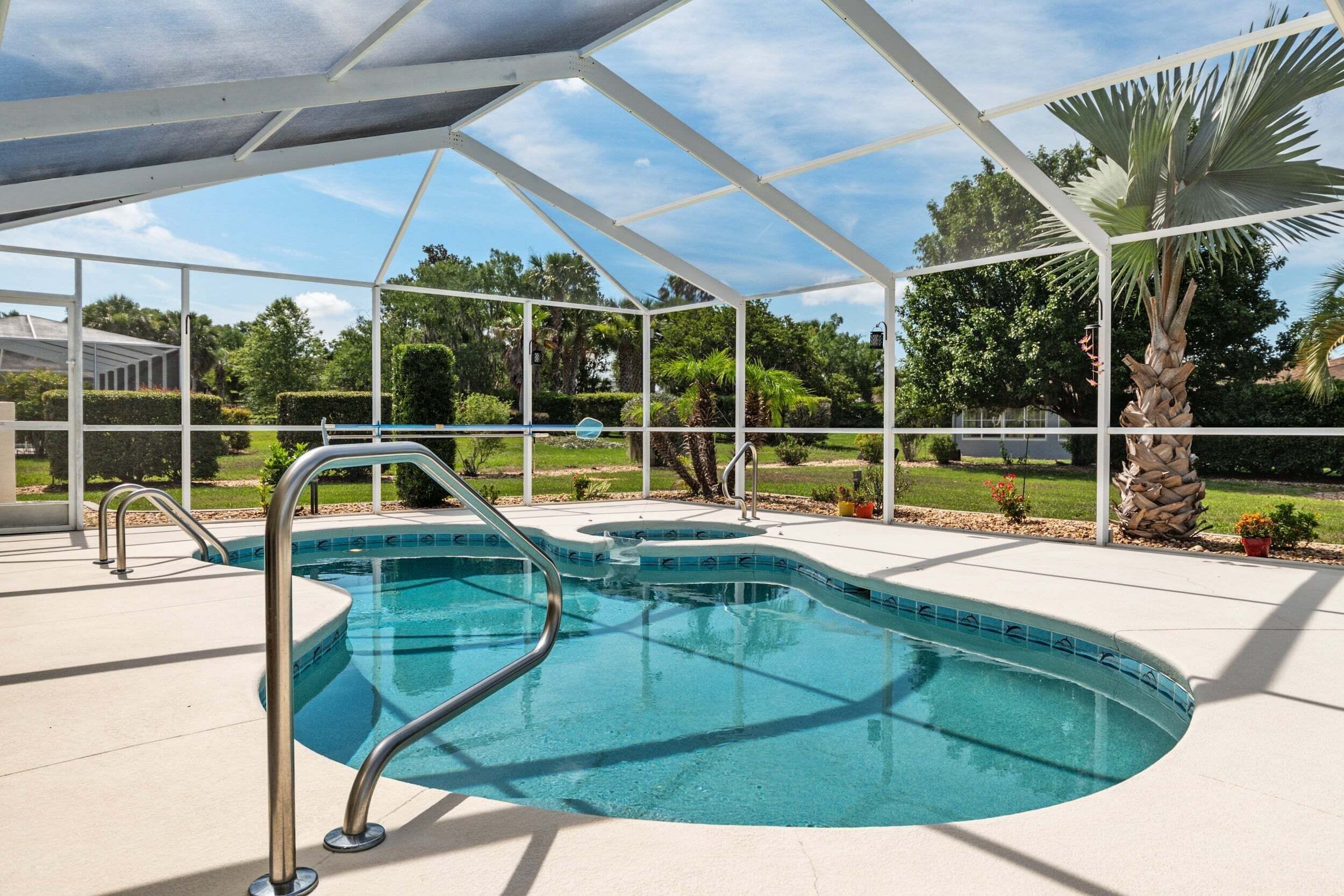 A swimming pool with a covered area, surrounded by greenery and a clear sky.