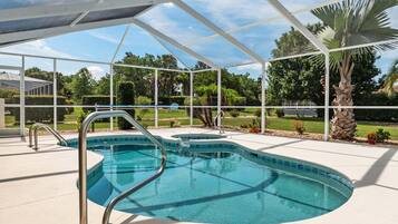 A swimming pool with a covered area, surrounded by greenery and a clear sky.
