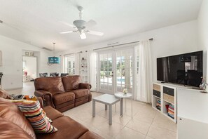 A living room with a brown leather sofa, a white coffee table, a ceiling fan, and a television on a white stand. - Family Villa Bettina - Recently Remodeled 2 Bedroom Home by RedAwning (Inverness)