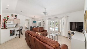 A modern living room with a brown leather sofa, a dining area with a white table and chairs, a kitchen with white cabinets, and a ceiling fan. - Family Villa Bettina - Recently Remodeled 2 Bedroom Home by RedAwning (Inverness)