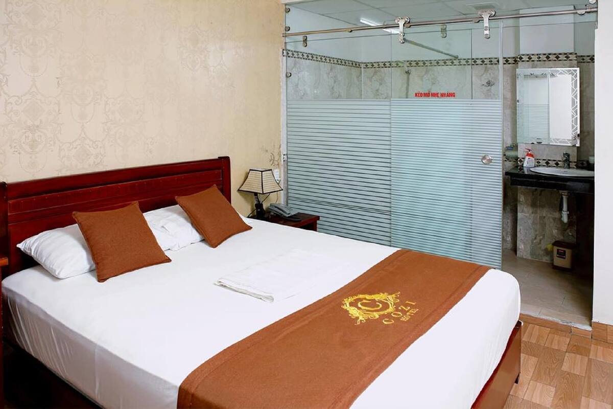 A hotel room with a bed, a nightstand, a lamp, a bathroom with a sink, and a mirror.