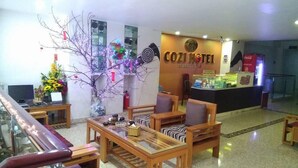 A lobby with wooden furniture, a reception desk, and a decorative tree. - Cozi Hotel (Hai Phong)