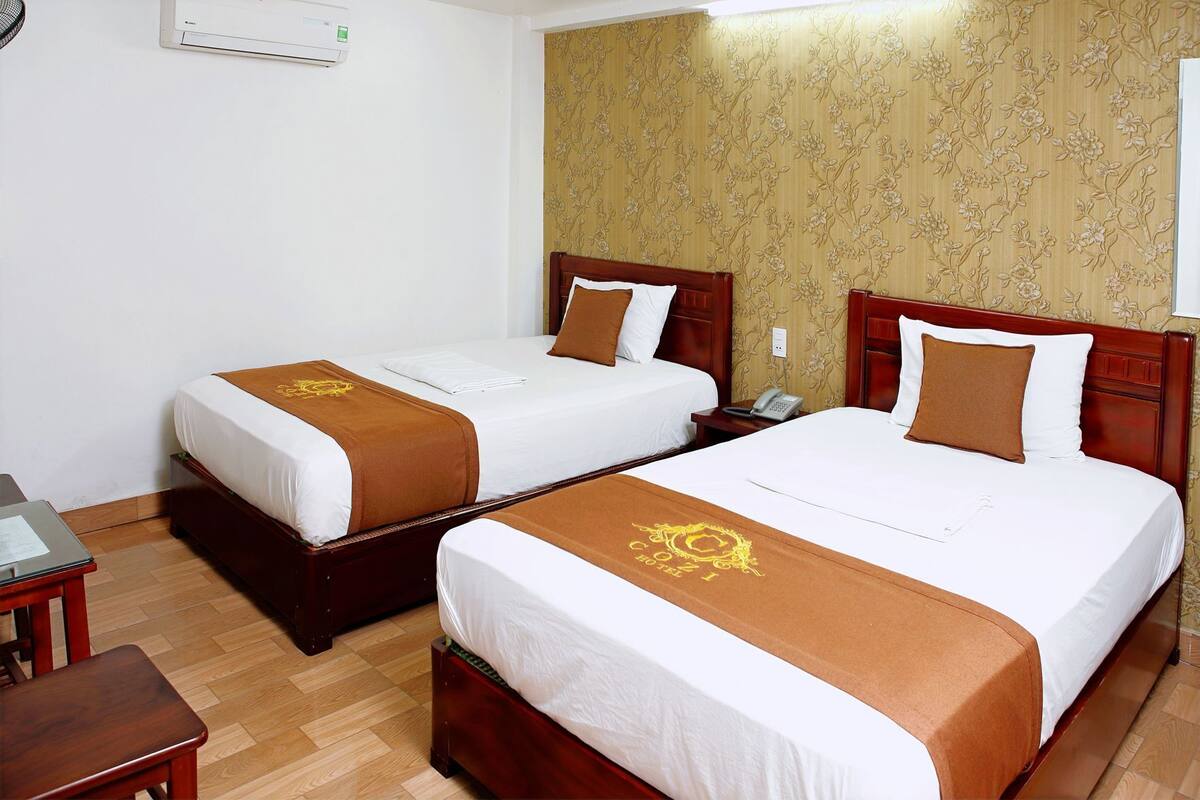 A hotel room with two beds, a wooden nightstand, a telephone, and a wall-mounted air conditioning unit.