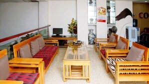 A room with wooden furniture, including sofas and tables, arranged around a central table. - Cozi Hotel (Hai Phong)