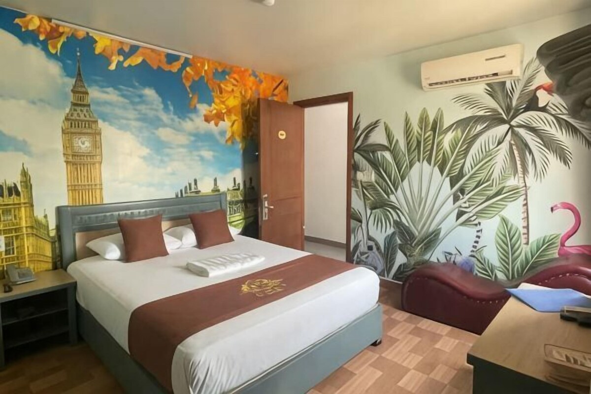 Habitación de hotel con una cama grande, una mesita de noche, un escritorio, una silla, un mural en la pared y una puerta.