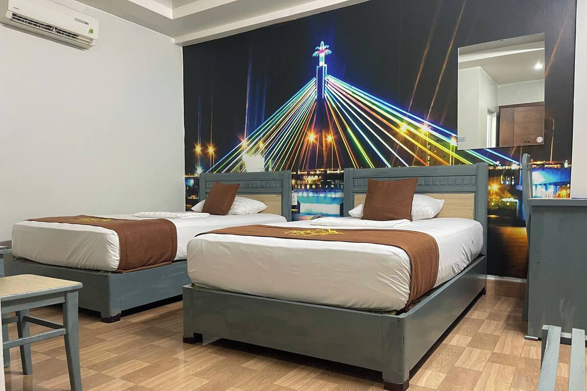A hotel room with two beds, a nightstand, a chair, and a wall mural of a cityscape at night.