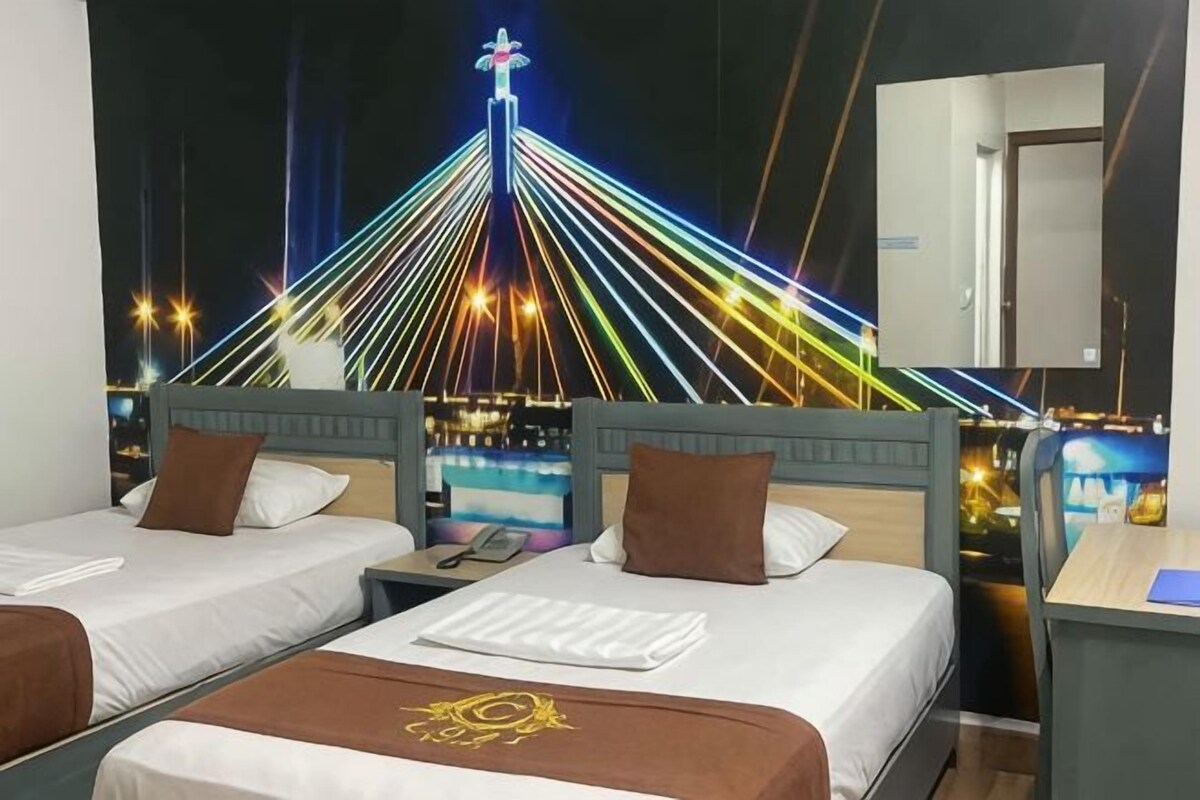 A hotel room with two beds, a desk, and a view of a bridge with lights.