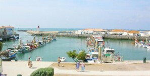 A harbor with boats docked, a lighthouse, and a building with 'SNM' signage. - Hôtel Restaurant L'Ecailler (Saint-Pierre-d'Oleron)