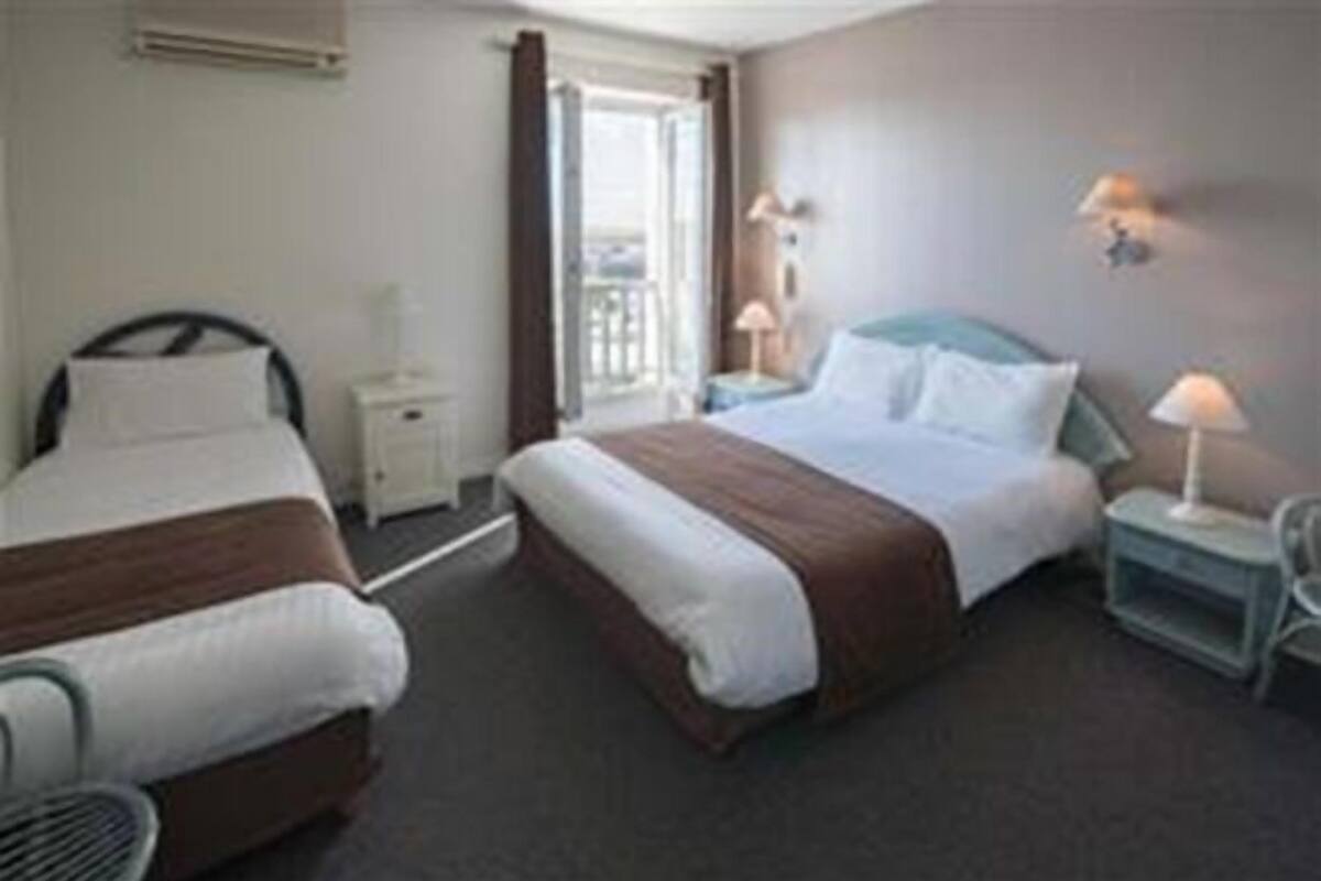 A hotel room with two beds, a window, a nightstand, and a lamp.