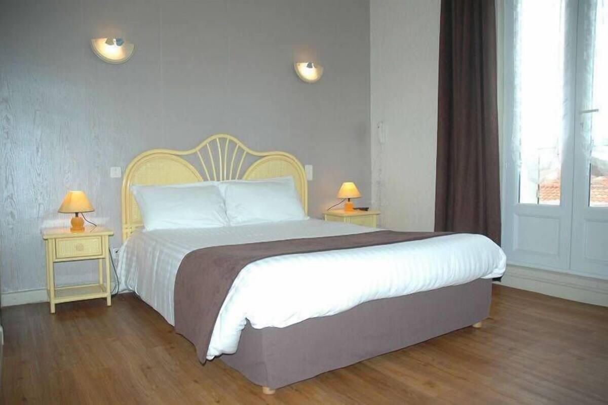 A single bed with a headboard, two bedside lamps, and a window with curtains.