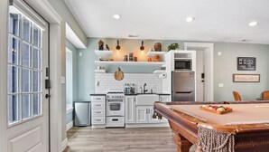 A spacious kitchen with white cabinets, a built-in oven, and a microwave. There is a wooden pool table in the foreground. - Film-featured, sleeps 18, hot tub, fire pit, decks (Heber City)