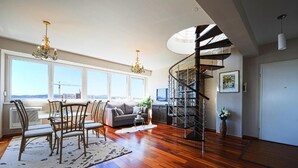 A spacious living area with a wooden floor, a dining set, a sofa, and a spiral staircase. - Sunset Penthouse Apartment with Hot Tub (Zadar)