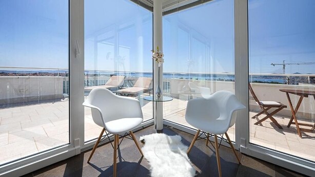 A balcony with white chairs and a glass table, overlooking a cityscape and the sea. - Sunset Penthouse Apartment with Hot Tub (Zadar)