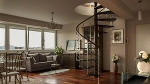 A modern living room with a spiral staircase, a sofa, a dining area, and a view through large windows. - Sunset Penthouse Apartment with Hot Tub (Zadar)